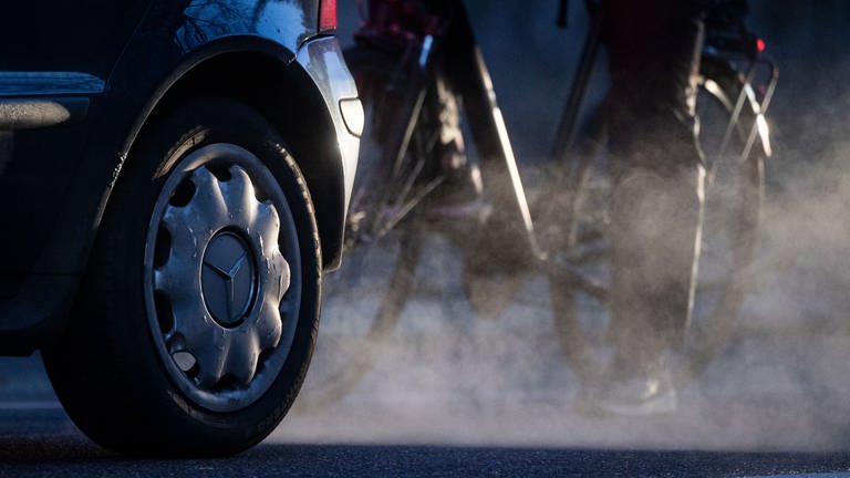 Ein Radfahrer steht neben einem Auto von Mercedes mit Dieselantrieb, dessen Abgase in der kalten Morgenluft sichtbar werden. (Foto: dpa Bildfunk, picture alliance/dpa | Marijan Murat)
